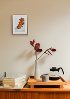 Small wooden table with a vase, books, and a coffee maker against a beige wall with a framed picture.