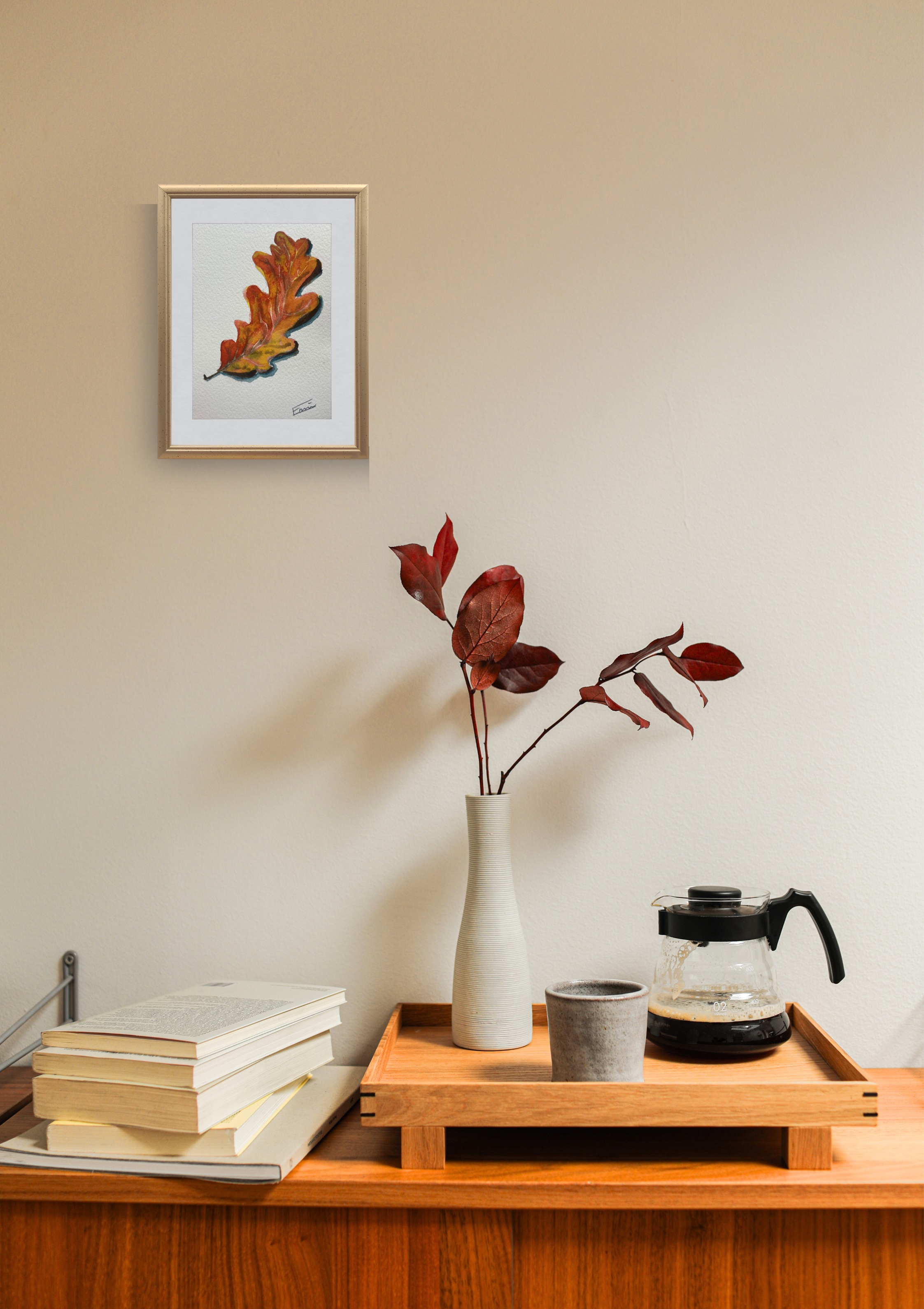 Small wooden table with a vase, books, and a coffee maker against a beige wall with a framed picture.